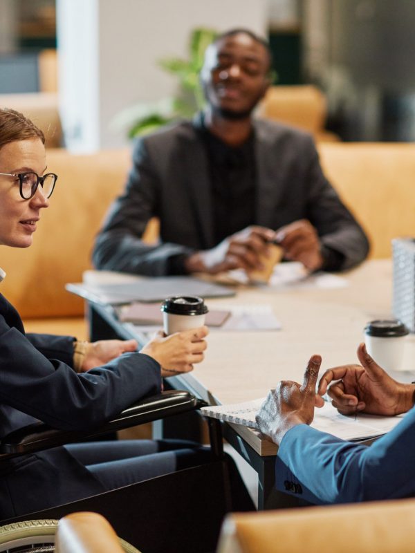 Side view portrait of successful businesswoman using wheelchair at meeting and talking to group of colleagues in modern office space